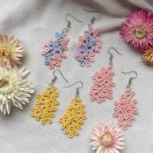 Peut inclure: Quatre paires de boucles d'oreilles en crochet délicates en jaune, rose et bleu clair. Les boucles d'oreilles sont toutes de designs différents et sont suspendues à des crochets argentés.