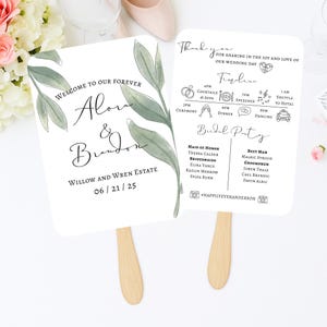 May include: Two white wedding fans with wooden handles. One fan features the text "Welcome to our Forever" and names "Alora & Brandon", with a date and venue. The other fan has a wedding timeline, bridal party details, and the text "Thank you".