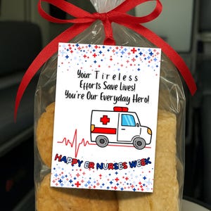 Peut inclure: Un sac en cellophane transparent noué avec un ruban rouge, contenant des pâtisseries et une étiquette. L'étiquette présente une illustration d'ambulance, le texte "Your Tireless Efforts Save Lives! You're Our Everyday Hero!" et "HAPPY ER NURSES WEEK".