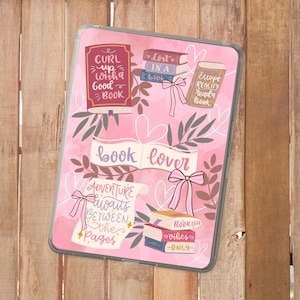 Op de afbeelding: Een roze tablet hoesje met een boekenliefhebber thema. De hoes heeft illustraties van boeken, strikken en zinnen als "Curl up with a good book" en "Adventure awaits between the pages."