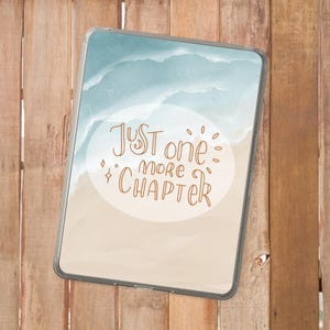 May include: A clear tablet case with a beach-themed wallpaper. The wallpaper features a light blue ocean and a sandy beach, with the text "Just one more chapter" in a brown script font.