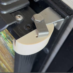 Può includere: Primo piano di un angolo di un'opera d'arte incorniciata. Un proteggi-angolo in plastica beige è fissato da una staffa metallica e una vite. La parola "KOOL" è visibile sulla cornice nera.