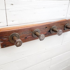 May include: A rustic wooden coat rack with four metal hooks. The hooks are made from large bolts with washers. The wood is a dark brown color and has a natural, weathered finish.