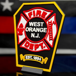 May include: A black, yellow, and red fire department emblem with the words "FIRE", "WEST ORANGE N.J. DEPT." and "EST. 1894". The emblem features a Maltese cross design with a fire hydrant and ladder.