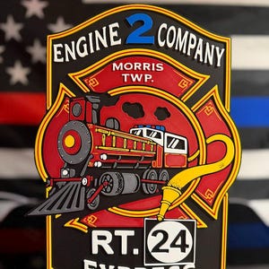 May include: A multi-layered wall sign featuring a red steam locomotive and a yellow fire hose nozzle. The text reads ENGINE 2 COMPANY, MORRIS TWP., and RT. 24 EXPRESS. The design is shaped like a Maltese cross with black, red, and yellow accents.