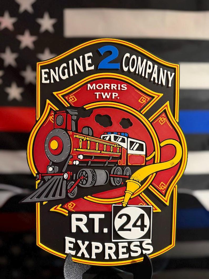 May include: A multi-layered wall sign featuring a red steam locomotive and a yellow fire hose nozzle. The text reads ENGINE 2 COMPANY, MORRIS TWP., and RT. 24 EXPRESS. The design is shaped like a Maltese cross with black, red, and yellow accents.