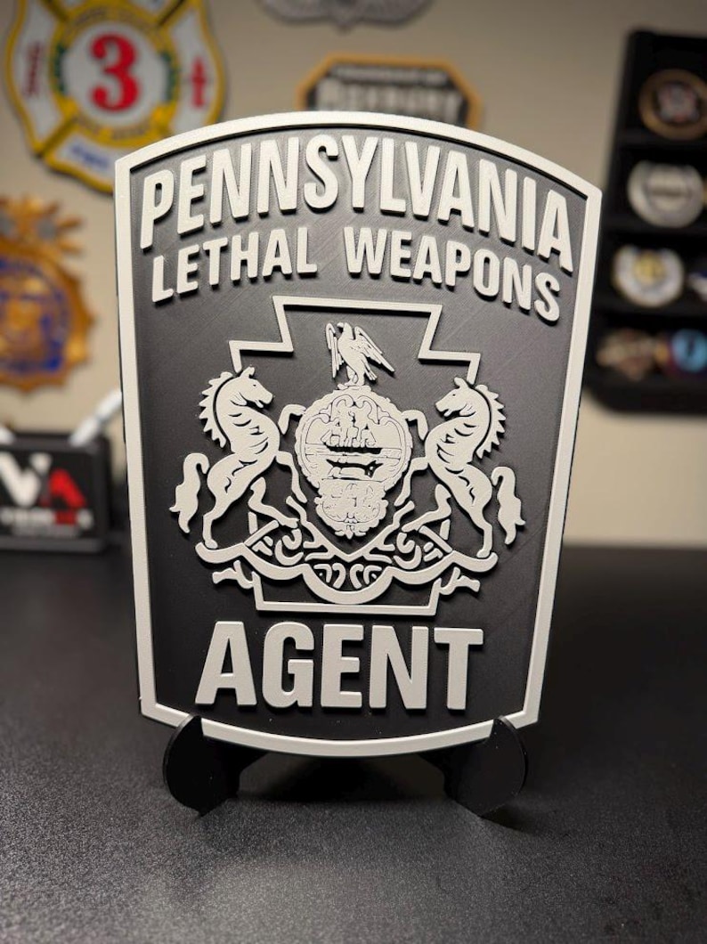 May include: A black and white shield-shaped plaque featuring the text PENNSYLVANIA LETHAL WEAPONS AGENT. The center displays the Pennsylvania state coat of arms with two horses, a central shield, and an eagle crest, all in a raised relief design.