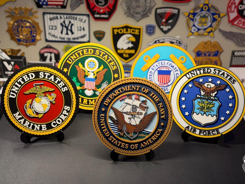 May include: A collection of five circular plaques representing United States military branches, including the Marine Corps, Army, Coast Guard, Navy, and Air Force. Each plaque features the official emblem, colors, and text of its respective branch.