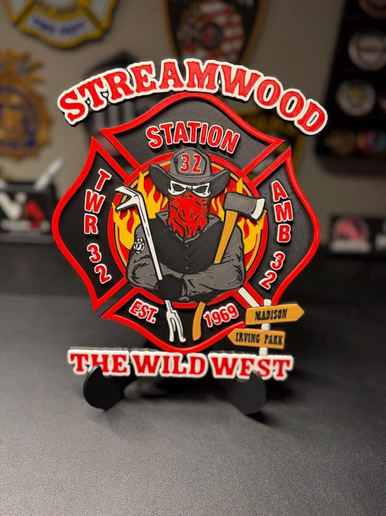 May include: A multi-layered wooden sign shaped like a Maltese cross featuring the text STREAMWOOD STATION, TWR 32, AMB 32, EST 1969, THE WILD WEST, MADISON, and IRVING PARK. The center depicts a figure in a cowboy hat, bandana, and skull mask.