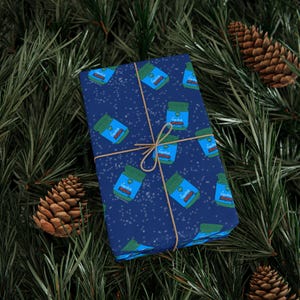 Könnte beinhalten: Ein rechteckiges Geschenkpaket in dunkelblauem Papier mit einem wiederkehrenden Muster aus kleinen grünen Tiegeln mit der Aufschrift VapoRub, umwickelt mit dünner beiger Schnur. Das Papier hat ein dezentes weißes Sprenkelmuster auf der Oberfläche.