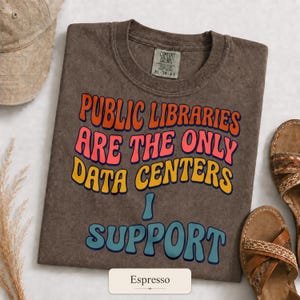 以下が含まれることがあります： PUBLIC LIBRARIES ARE THE ONLY DATA CENTERS I SUPPORTというテキストが波打つようなマルチカラーの文字でプリントされた、ブラウンの半袖クルーネックTシャツ。首の内側にはComfort ColorsのラベルとXLサイズのタグが付いています。
