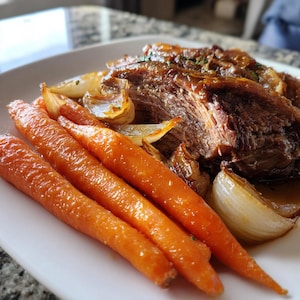 May include: A plate of roasted meat with caramelized onions and glazed carrots. The meat is a rich brown color, and the carrots are bright orange. The onions have a golden-brown hue, and the dish is served on a white plate.