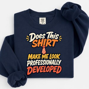 Puede incluir: Una sudadera azul marino de manga larga con un estampado gráfico que incluye el texto Does This SHIRT MAKE ME LOOK PROFESSIONALLY DEVELOPED en letras blancas, amarillas y naranjas, junto a un pequeño icono de corbata a rayas rojas y blancas.