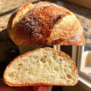 Puede incluir: Un pan artesanal recién horneado, dorado con una corteza crujiente y un interior suave y aireado. La parte superior está espolvoreada con harina, y una rebanada revela una textura ligera y porosa. El pan está listo para comer.