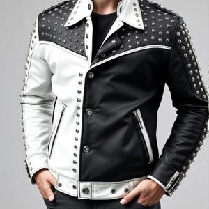 Op de afbeelding: Een zwart en wit leren jack met zilveren studs. Het jack heeft een knoopsluiting en twee zakken.