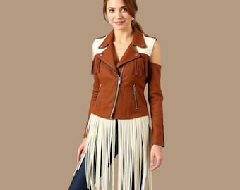 May include: Brown leather jacket with white shoulder accents and long cream-colored fringe. The jacket has a zipper closure and fringe detailing on the sleeves. The model is wearing blue jeans and brown boots.