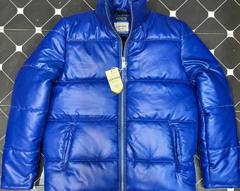 May include: A vibrant blue puffer jacket with a high collar and a full-length zipper. The jacket features horizontal quilted panels and two side pockets. A tag with the word "LEATHER" is attached to the zipper. The jacket is made of a shiny material.
