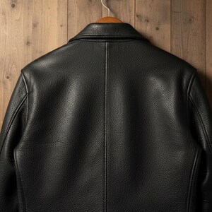 May include: A black leather jacket hangs on a wooden hanger against a wood-paneled background. The jacket's back is visible, showcasing the textured leather and stitching details. The collar is turned up, and the jacket appears to be a classic style.