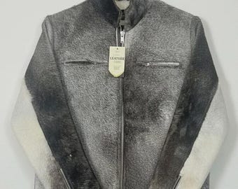 Peut inclure: Veste en cuir grise et blanche avec une fermeture éclair intégrale et deux poches avant. La veste a un col montant et une étiquette qui indique "Leather Goods". Les manches ont un design blanc et noir contrasté.