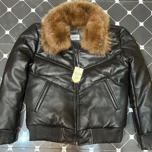 Peut inclure: Veste en cuir noir avec un col en fourrure marron. La veste a une fermeture éclair, des poignets et un ourlet côtelés. Elle possède deux poches avant et une étiquette indiquant "LEATHER".