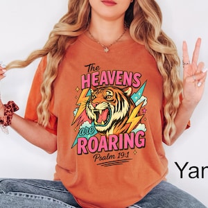 May include: Orange t-shirt with a graphic of a roaring tiger, lightning bolts, and the text "The Heavens are Roaring" and "Psalm 19:1". The tiger is orange, black, and white. The text is in pink and green.