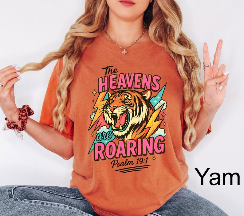 May include: Orange t-shirt with a graphic of a roaring tiger, lightning bolts, and the text "The Heavens are Roaring" and "Psalm 19:1". The tiger is orange, black, and white. The text is in pink and green.