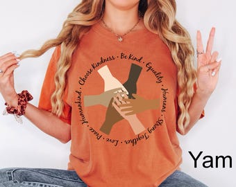 May include: Orange t-shirt with a graphic of hands in different skin tones, encircled by text that reads "Choose Kindness, Be Kind, Equality, Humans, Strong Together, Love, Peace, Humankind." The word "Yam" is printed in black.