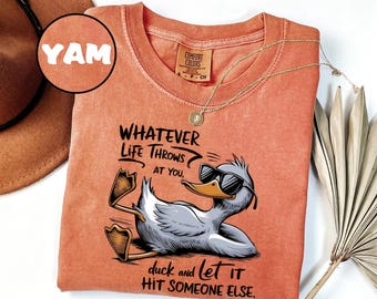 Könnte beinhalten: Orangefarbenes Comfort Colors T-Shirt mit einer Grafik einer Ente mit Sonnenbrille und dem Text "WHATEVER LIFE THROWS AT YOU, duck and let it HIT SOMEONE ELSE." Eine goldene Halskette und ein brauner Hut sind ebenfalls zu sehen.