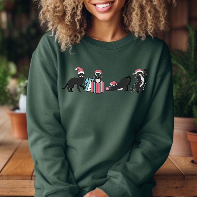 May include: Dark green sweatshirt featuring a graphic of black cats wearing Santa hats. The cats are interacting with a wrapped gift. The sweatshirt is made of a soft material and is suitable for the holiday season.