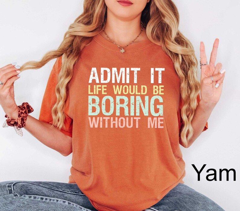 Op de afbeelding: Een oranje t-shirt met de tekst "ADMIT IT LIFE WOULD BE BORING WITHOUT ME" in wit, groen en geel. Het shirt heeft een ronde hals en korte mouwen.