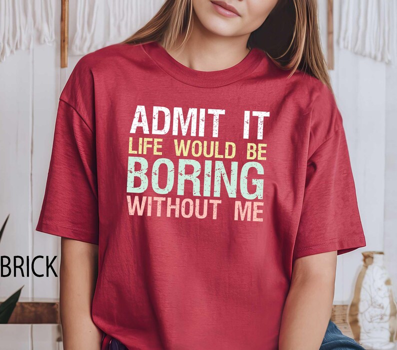 Op de afbeelding: Baksteenrood T-shirt met de tekst "ADMIT IT LIFE WOULD BE BORING WITHOUT ME" in wit, geel en groen. Het shirt heeft korte mouwen en een ronde hals.