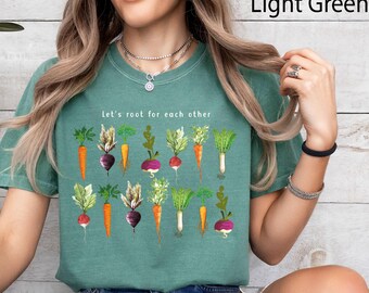 May include: A light green t-shirt with the text "Let's root for each other" and a graphic of various vegetables, including carrots, radishes, and turnips.