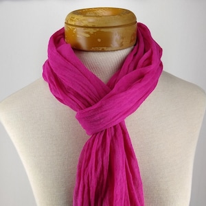 May include: A bright pink, lightweight scarf made of a soft, gauzy fabric. The scarf is draped over a mannequin's neck and shoulders.