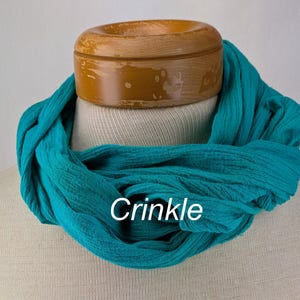 May include: A teal blue crinkle scarf, folded and displayed on a wooden mannequin head.