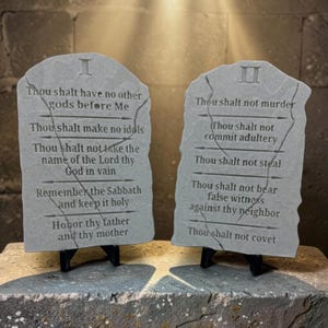 May include: Two gray stone tablets featuring engraved text of the Ten Commandments. The first tablet is marked with a Roman numeral I and the second with a Roman numeral II. Each tablet displays five distinct lines of text separated by arrow icons.