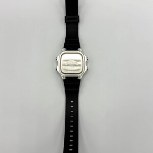 May include: A black digital wristwatch with a silver face and a black rubber strap. The watch has a rectangular face and a buckle closure. The strap is approximately 9 inches long.