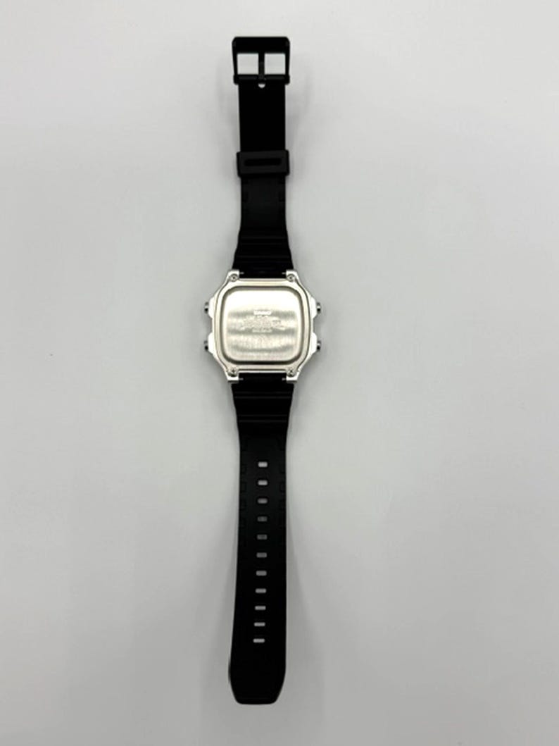 May include: A black digital wristwatch with a silver face and a black rubber strap. The watch has a rectangular face and a buckle closure. The strap is approximately 9 inches long.