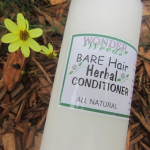 May include: A white bottle of "Wonder Weeds" Bare Hair Herbal Conditioner with a green and white label. The bottle is next to yellow flowers and wood chips.