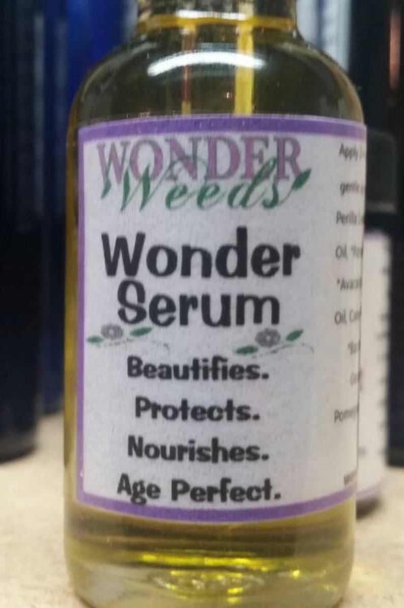 May include: A small glass bottle with a yellow liquid inside. The label is white with purple trim and reads "WONDER Weeds Wonder Serum Beautifies. Protects. Nourishes. Age Perfect."