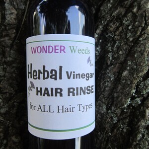 May include: A glass bottle with a white label that reads "WONDER Weeds Herbal Vinegar HAIR RINSE for ALL Hair Types".