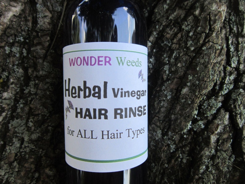 May include: A glass bottle with a white label that reads "WONDER Weeds Herbal Vinegar HAIR RINSE for ALL Hair Types".