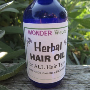 Op de afbeelding: Een blauwe glazen fles met een wit etiket waarop staat "WONDER Weeds Herbal HAIR OIL for ALL Hair Types with Nettle, Rosemary, & Calendula".