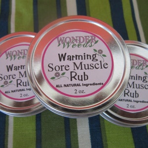 Puede incluir: Tres latas plateadas con etiquetas blancas y letras rosas. Las etiquetas dicen "Wonder Weeds Warming Sore Muscle Rub" y "All Natural Ingredients 2 oz."