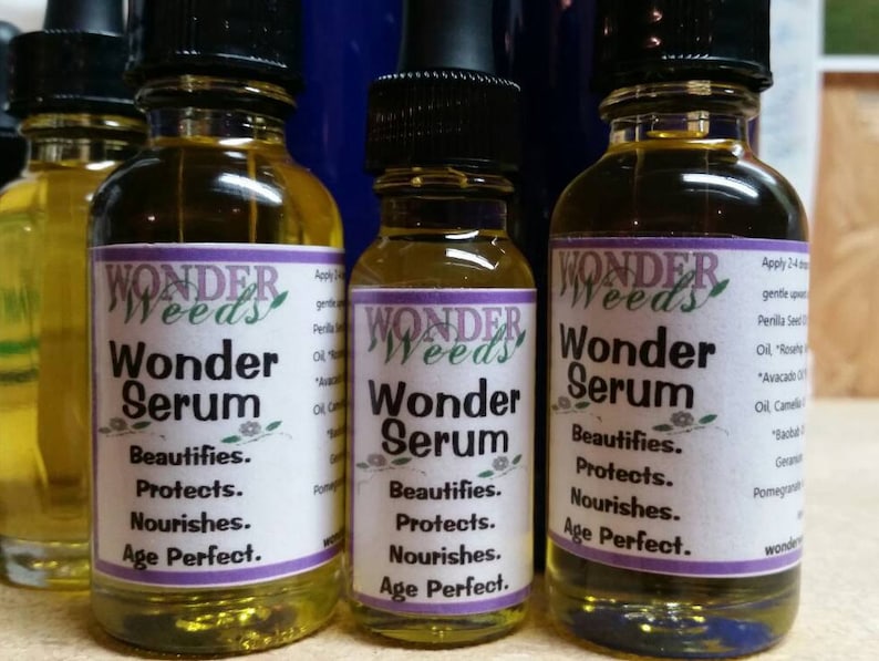 May include: Four amber glass bottles with a clear liquid inside. The bottles have purple labels with the text "Wonder Weeds" and "Wonder Serum" on them. The labels also list the benefits of the serum, including "Beautifies", "Protects", "Nourishes", and "Age Perfect".