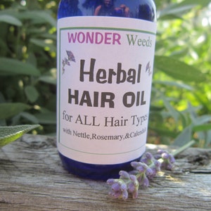 Op de afbeelding: Een blauwe glazen fles met een wit etiket waarop staat "WONDER Weeds Herbal HAIR OIL for ALL Hair Types with Nettle, Rosemary, & Calendula".