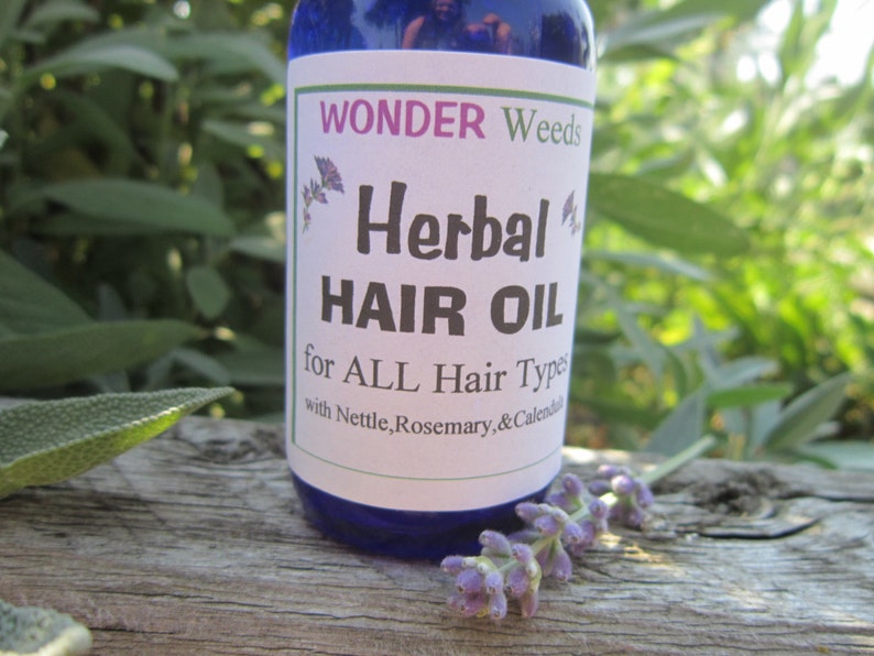 Op de afbeelding: Een blauwe glazen fles met een wit etiket waarop staat "WONDER Weeds Herbal HAIR OIL for ALL Hair Types with Nettle, Rosemary, & Calendula".
