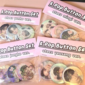Könnte beinhalten: Vier Sets von K-Pop-Button-Sets, jeweils verpackt in einer transparenten Plastiktüte mit einem rosa Header. Jedes Set enthält drei runde Knöpfe mit Bildern von K-Pop-Bandmitgliedern. Die Header lauten "K-Pop Button Set" mit dem Namen des Bandmitglieds.