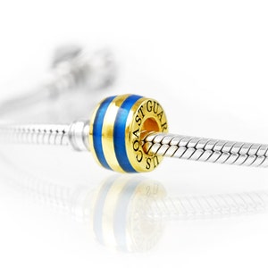 May include: A gold and blue bead with the text "U.S. COAST GUARD" on a silver bracelet. The bead has blue stripes and gold accents. The bracelet is made of silver and has a snake chain design.