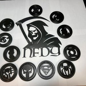 May include: Black 3D-printed coasters featuring various superhero and comic book logos, including Superman, Spider-Man, and the Punisher. A large black and white graphic of the Grim Reaper with the word "NFDG" is also present.