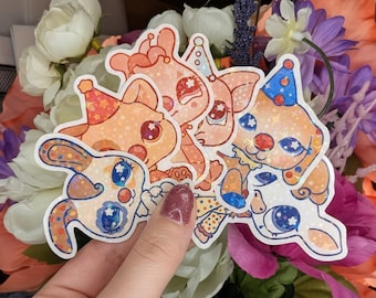 May include: A collection of colorful, glittery stickers featuring cartoon animal characters wearing party hats. The stickers have a whimsical design with stars and polka dots, and are in shades of orange, pink, and blue.